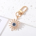 Detail of golden Evil Eye keychain with blue sunburst design on white marble surface - Sunburst Shape Grey Eye Gold