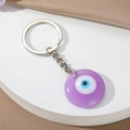 Detail eines lila Harz-Evil-Eye-Schlüsselanhängers mit silbernem Ring auf Satinhintergrund - Lila