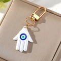 Llavero Hamsa dorado con dije de ojo turco blanco y azul sobre caja de exhibición - Blanco