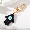 Vista macro de la mano de Fátima negra con ojo azul y cierre de metal dorado - Negro