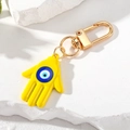 Detalle del llavero mano de Fátima amarillo con ojo azul sobre un fondo de piedra texturizada - Amarillo