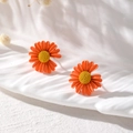 Nahaufnahme von orangen mattierten Gänseblümchen-Ohrringen auf einem weißen Tablett - Gänseblümchen-Stil / Orange