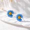 Detailansicht der matten blauen Gänseblümchen-Ohrstecker mit gelben Details auf Stoff - Gänseblümchen-Stil / Blau