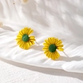 Detailaufnahme gelber Gänseblümchen-Ohrstecker mit grüner Mitte auf weißem Stoff - Gänseblümchen-Stil / Gelb