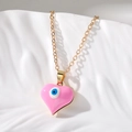 Detalle de un colgante de corazón rosa con ojo turco y cadena dorada sobre fondo blanco - Rosa