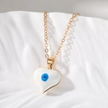 Dettaglio della collana dorata a cuore con malocchio su vassoio in ceramica - Bianco