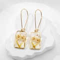 Detailed macro shot of handmade resin square earrings with yellow dried flowers and gold foil - Wheat Flower