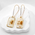 Macro shot of rectangular resin earrings with real dried daisies and gold foil flakes - White Daisy