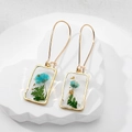 Macro shot of rectangular resin earrings with blue dried flowers and gold foil elements - Green Leaf Blue Flower