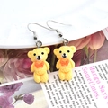 Gros plan de boucles d'oreilles ours en résine jaune avec nœud orange sur plat en porcelaine - Ours Jaune