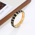 Detail of bohemian gold metal bangle with black enamel segments and hinged clasp closure - Gold + Black
