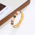 Detalle de un brazalete de bisagra dorado bohemio con patrones de esmalte tricolor - Oro & Café Arena