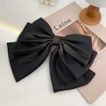 Detail view of a large black satin bow hair clip on a minimalist lifestyle magazine background - Black