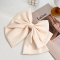 Detailed close-up of a large satin bow hair clip in champagne pink on a stylish table - White