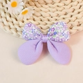 Detail of floral and purple fabric bow hair accessory on a rustic woven mat background - Purple