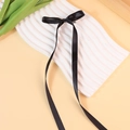 Elegant black satin bow hair clip with long ribbons on white wavy display stand - Black