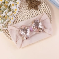 Elastic baby headband with a skin-pink sequin bow on a rustic woven background - Champagne