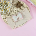 Creamy cotton baby headband featuring a bow with pink scalloped edges on a woven mat - Beige