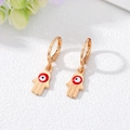 Pendientes dorados de Mano de Fátima con amuleto de ojo turco sobre fondo blanco texturizado - Ojo Rojo y Blanco Dorado