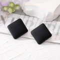 Detail showing a pair of matte black square stud earrings on a textured background - Black