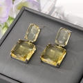 Elegantes pendientes cuadrados de plata con cristales amarillos sobre una caja gris - Beige