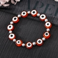 Détail du bracelet de perles Mauvais Oeil rouge avec perles argentées sur fond noir - Marron