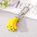 Realistic yellow banana cluster keychain with silver metal clip on a textured grey surface - Banana Keychain
