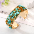 Detail of bohemian gold cuff with turquoise stones and gold pyramid studs on white surface - Blue Stone Bangle