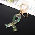 Detailed close-up of handmade acrylic keychain with green leaves and gold foil flakes - Ribbon Bow / Green Leaf