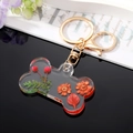 Détail du porte-clés en résine en forme d'os avec fleurs séchées rouges et fermoir doré - Fleur Orange