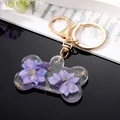 Détail d'un porte-clés en résine en forme d'os avec fleurs violettes et feuilles d'or - Fleur Violette