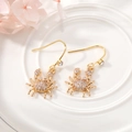 Detail of gold crab drop earrings with sparkling rhinestones on a white ceramic plate - Crab