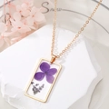 Gros plan d'un pendentif rectangulaire en résine avec fleurs séchées sur chaîne dorée - Hydrangée Violette (Fleur Violette n° 5)