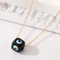 Nahaufnahme eines Harz-Evil-Eye-Würfels am Goldkettchen mit kunstvoller Karte im Bild - Schwarz