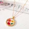 Détail d'un pendentif artisanal en résine avec fleurs séchées et bordure dorée - Fleurs Rouges et Jaunes