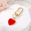 Detalle de un mosquetón dorado con colgante de corazón rojo sobre base decorativa - Rojo (K60)