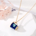Détail d'un collier doré avec pendentif tasse bleu foncé et motif cœur sur un socle en pierre - Gobelet Bleu Foncé Coeur Bleu