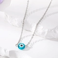 Blue resin evil eye pendant necklace with a fine silver-tone metal chain on a stone - Blue Eye