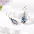 Detail of teardrop silver earrings with blue dried flowers on white stone background - Blue Earrings