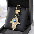 Nahaufnahme von goldenem Hamsa-Hand Schlüsselanhänger mit blauem Auge und Karabiner - Goldfarbene Kleine Handfläche