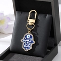Makroaufnahme von Hamsa-Hand-Schlüsselanhänger mit blauem Emaille und Strasssteinen - Goldene Multi-Augen-Hamsa Blau