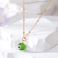 Close-up of golden necklace with green Evil Eye bead pendant on white stone - Green
