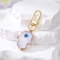Hamsa hand evil eye keychain with gold trim on white stone display for accessories - White Mickey Glove Style