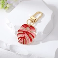 Détail du porte-clés feuille de monstera rouge et rose avec fermoir doré sur pierre - Feuille Rouge et Rose