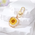 Detail of a handmade resin keychain featuring a real yellow dried flower with gold border - Yellow Flower