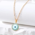 Close-up of golden evil eye necklace with mint green enamel charm on white stone blocks - Small Round Eye / Light Blue