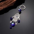 Etnische zilveren Hamsa-hand sleutelhanger met blauwe Evil Eye kralen op een donkere spiegel - Zilveren Hand van Fatima