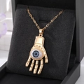 Macro d'un pendentif main dorée de style bohème avec un œil bleu serti au centre - Œil Gris Paume Dorée