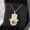 Vue détaillée du pendentif Main de Fatma dorée avec œil bleu sur support en velours noir - Œil Gris Grande Main De Fatima Dorée