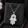 Detaillierte Makroansicht von Hamsa-Anhänger mit Strass und blauem Auge auf Samt - Silber Blau Rosa Auge